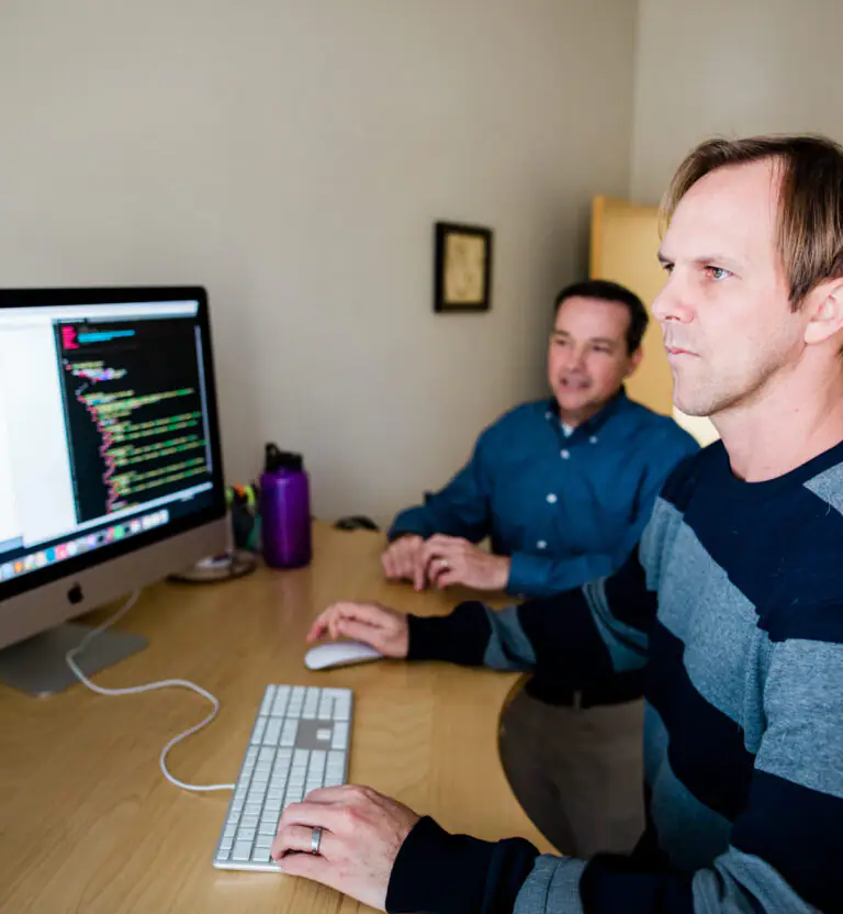 Web developers reviewing website code during front-end and back-end development on a desktop computer.